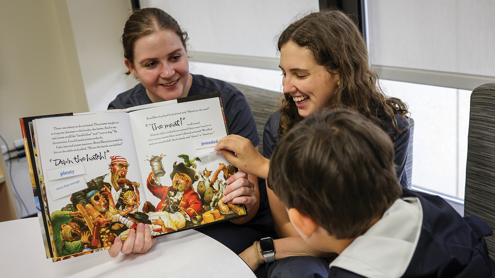 A Camp Success client reads a book wit two graduate student clinicians.