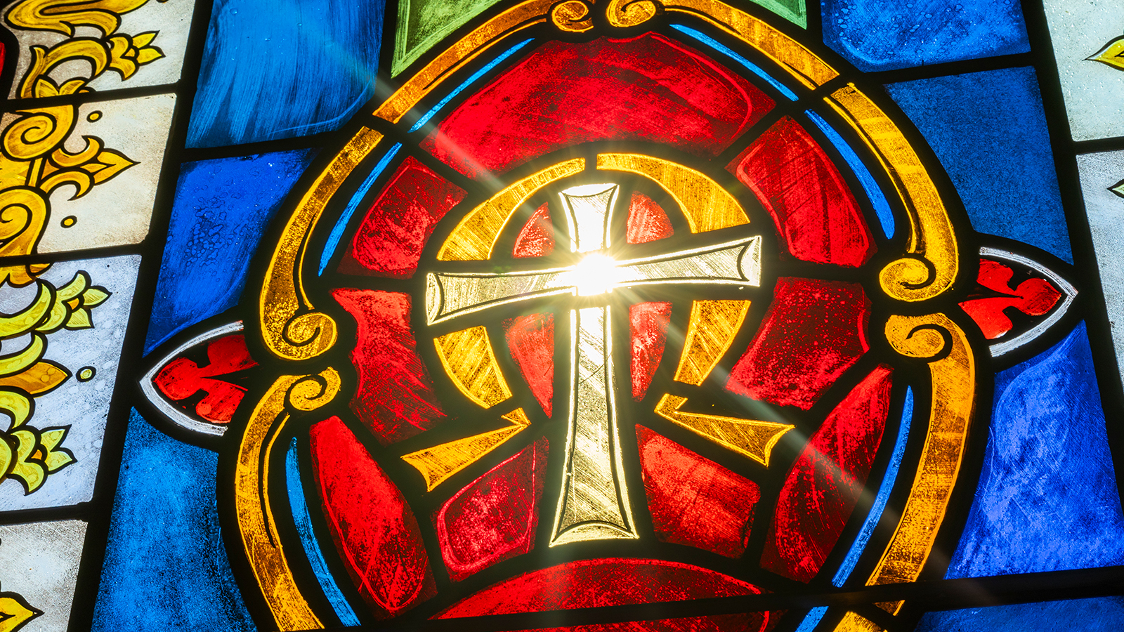 Light shines through a stained-glass window with a cross design.