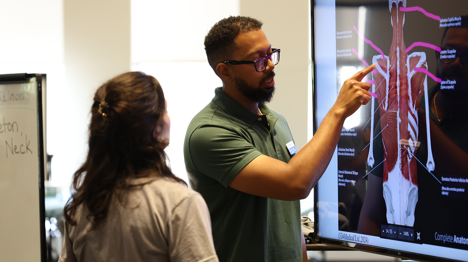 Two people use a large digital touchscreen during occupational therapy lab immersion instruction 