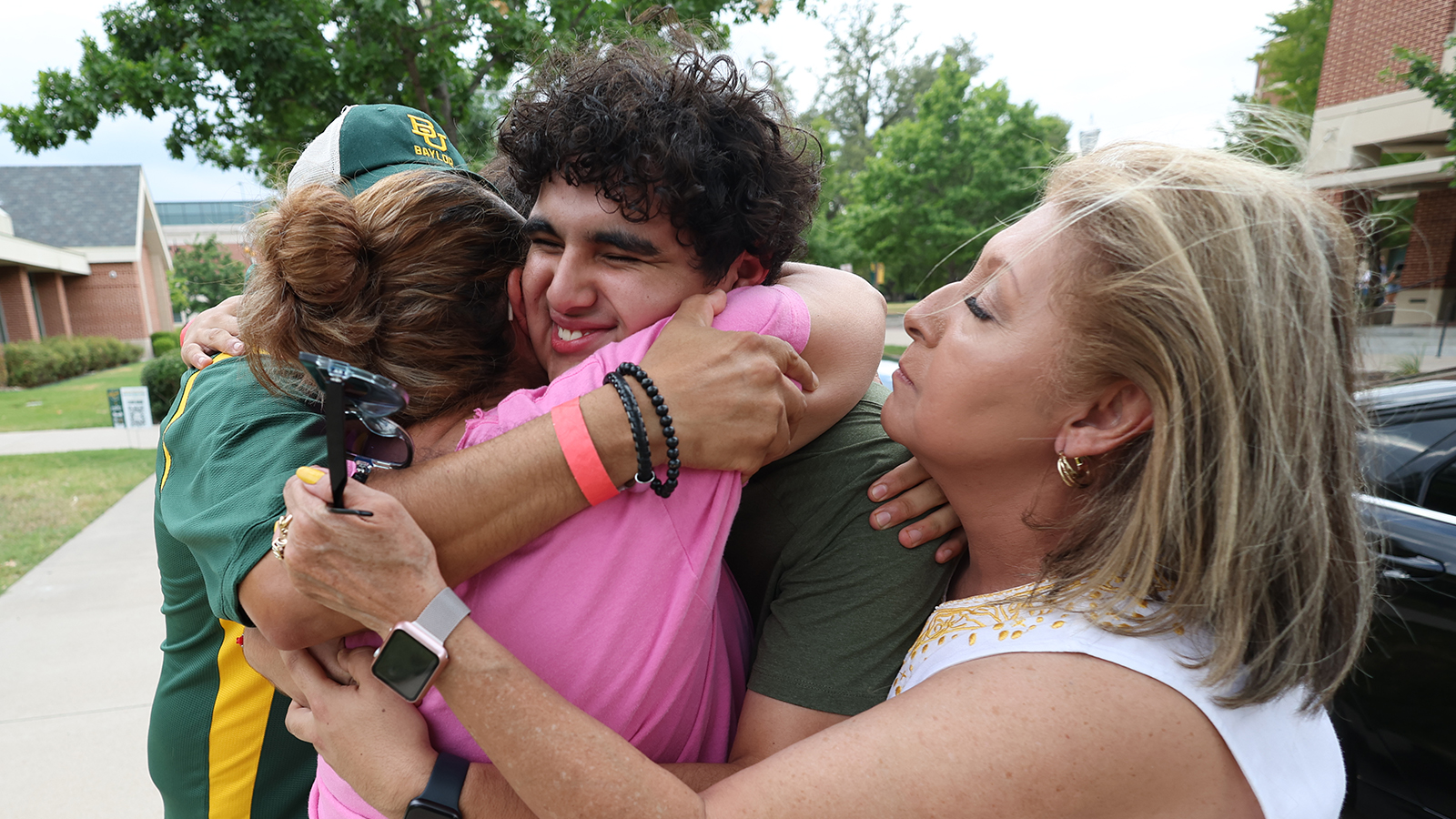 A family hugs their student outside, with emotion on their faces.