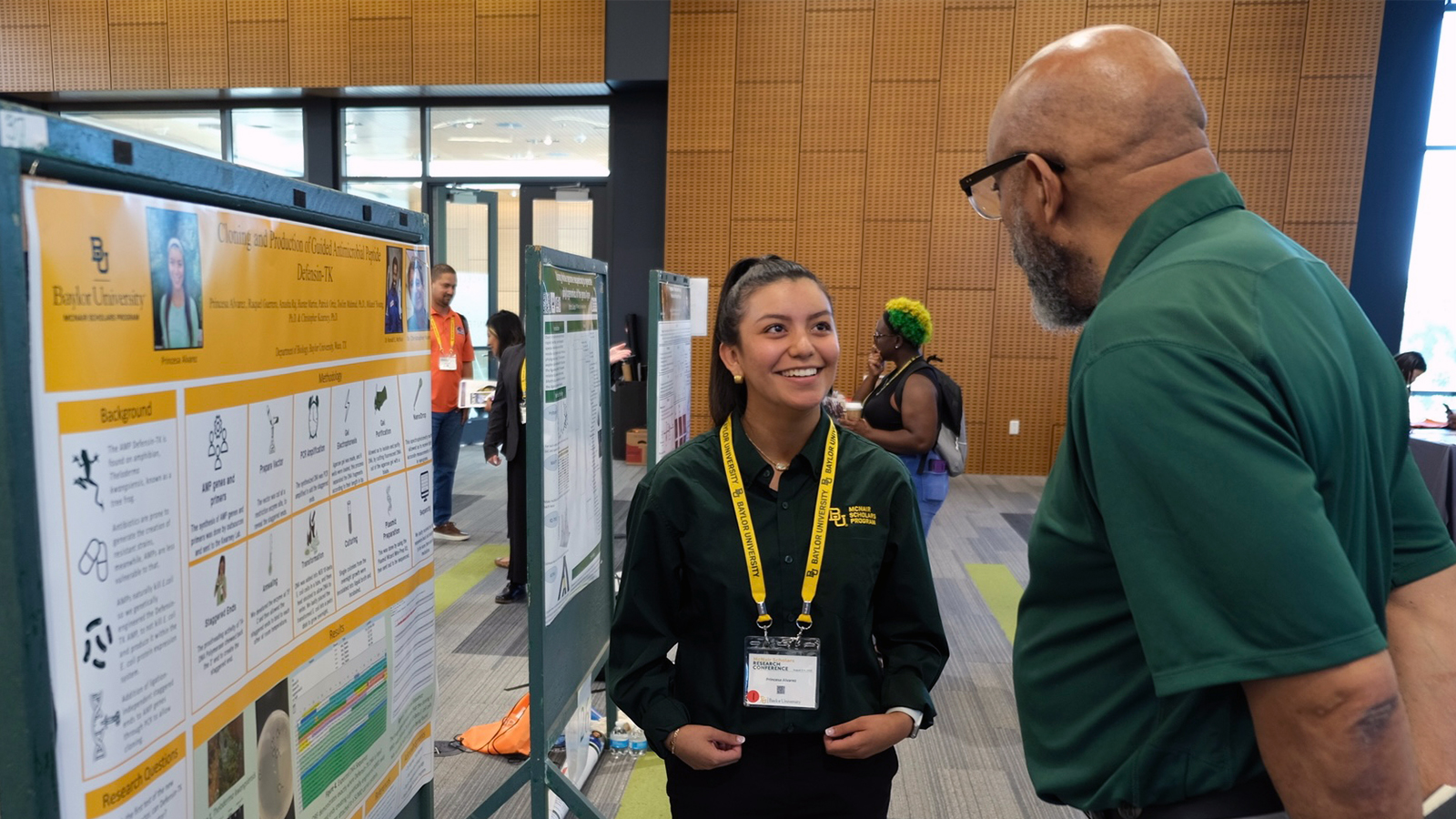 Baylor student Princesa Alvarez discusses her research poster with a man in a green polo. 