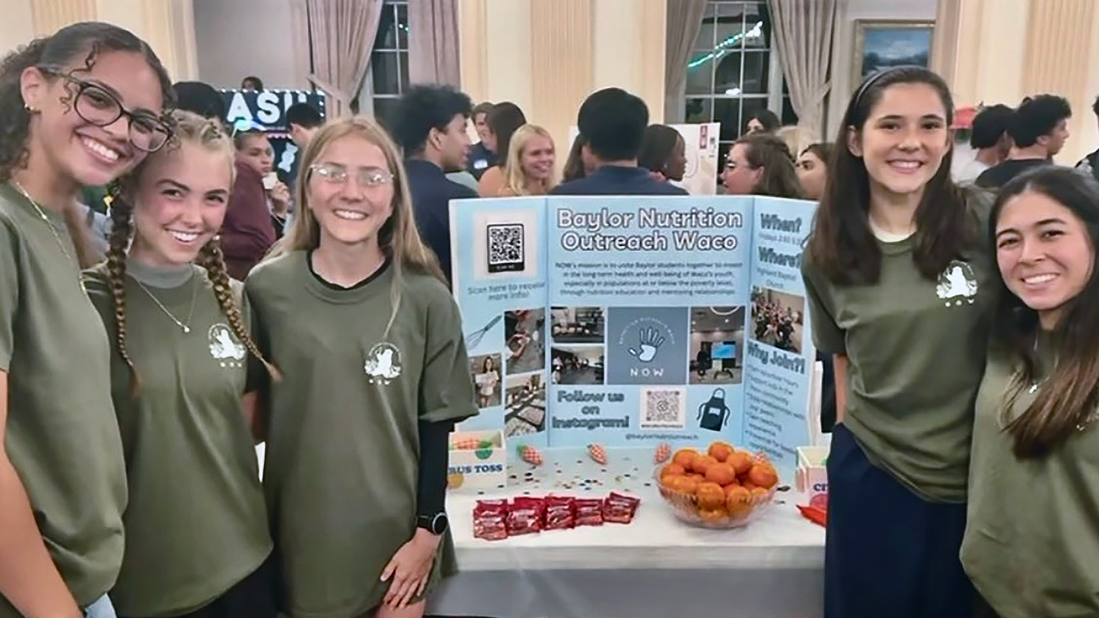 Five Nutrition Outreach Waco volunteers share nutritional information on a poster with fruit on the table