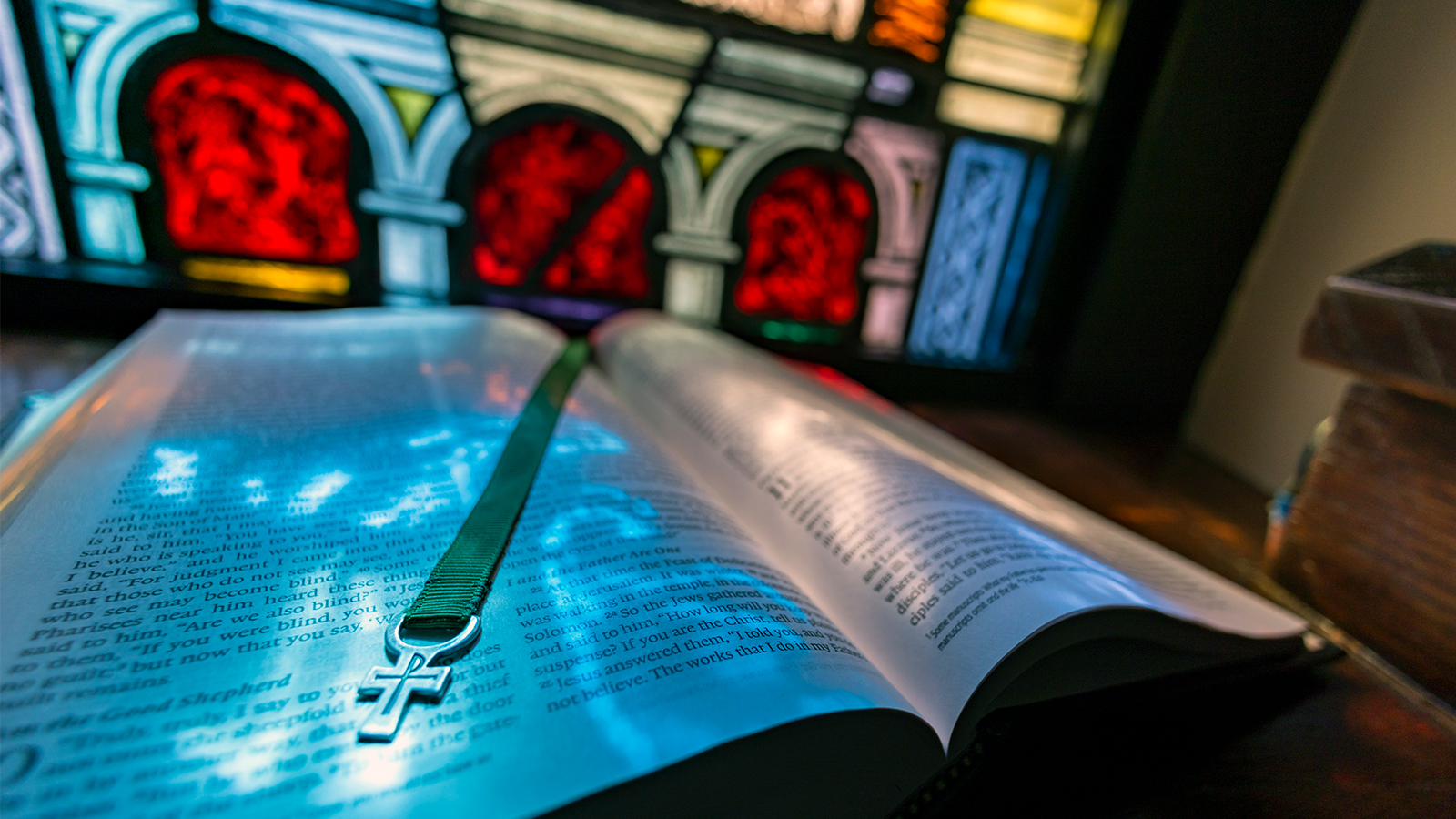 Light from stained glass window shines on open Bible. 