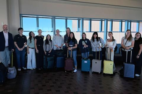 Thirteen individuals pose with suitcases at the airport on trip to New Mexico.