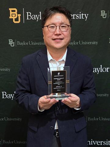 Dr. Jay Yoo poses with award in front of Baylor University branded backdrop.