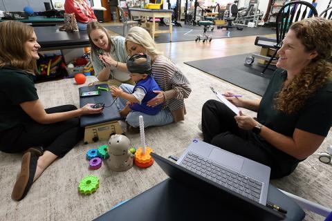 A young child plays with colorful toys during play-based activities as researchers interact and take notes.
