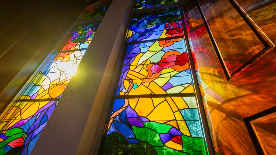 Light shines through a stained glass window, reflecting colors onto wood.