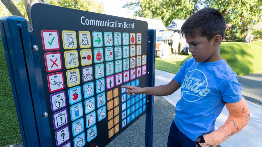 A young boy points to symbols on a communication board at an inclusive playground.