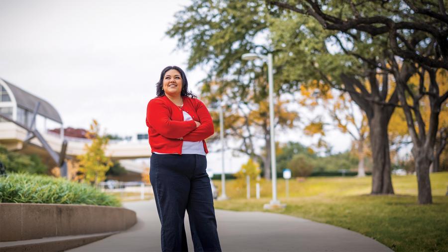 A woman, wearing a red cardigan and black pants, looks toward sky while standing in a park.