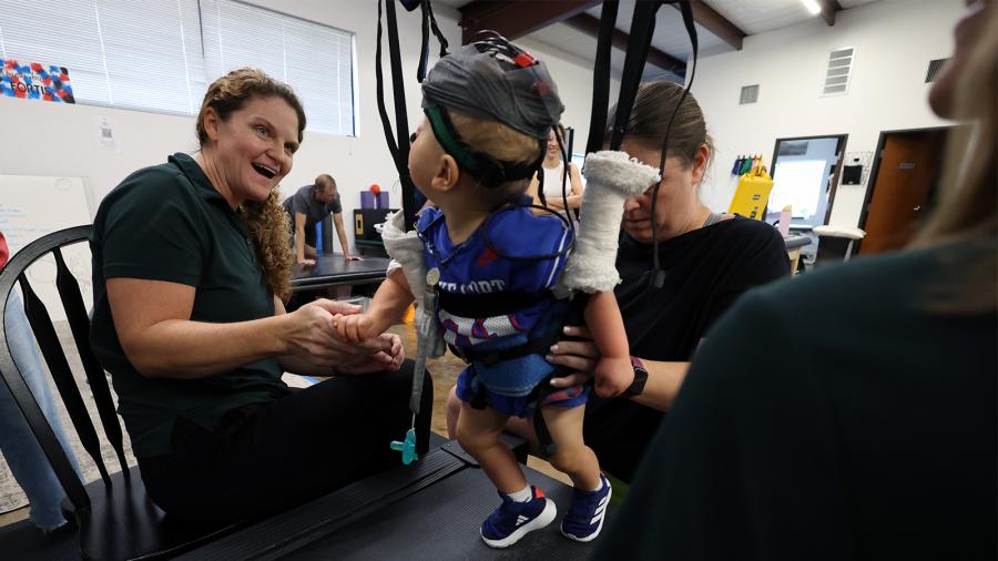 Three physical therapists work with a young child engaging in partial body weight-supported treadmill training.